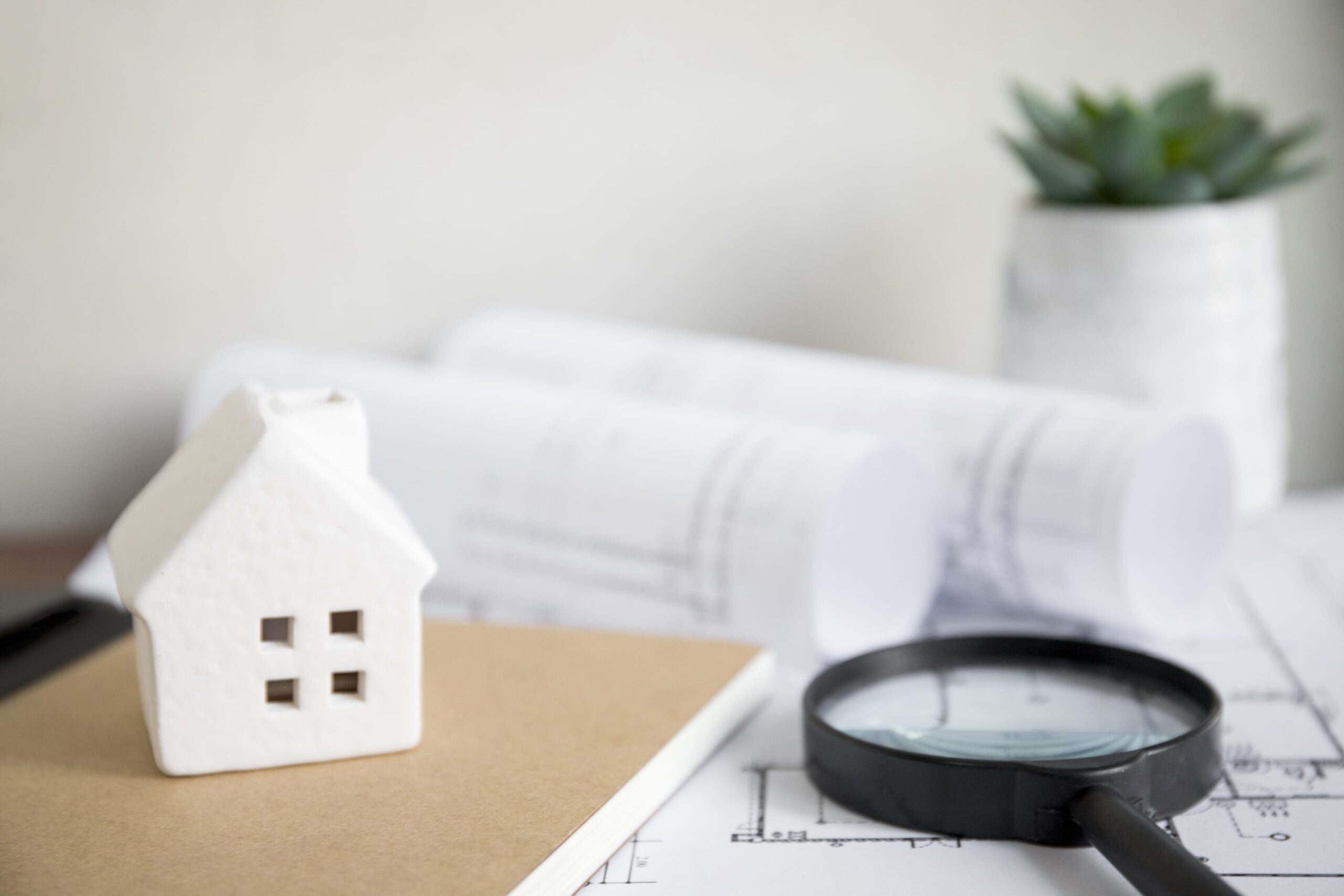 house-and-notebook-near-magnifying-glass-and-drafts